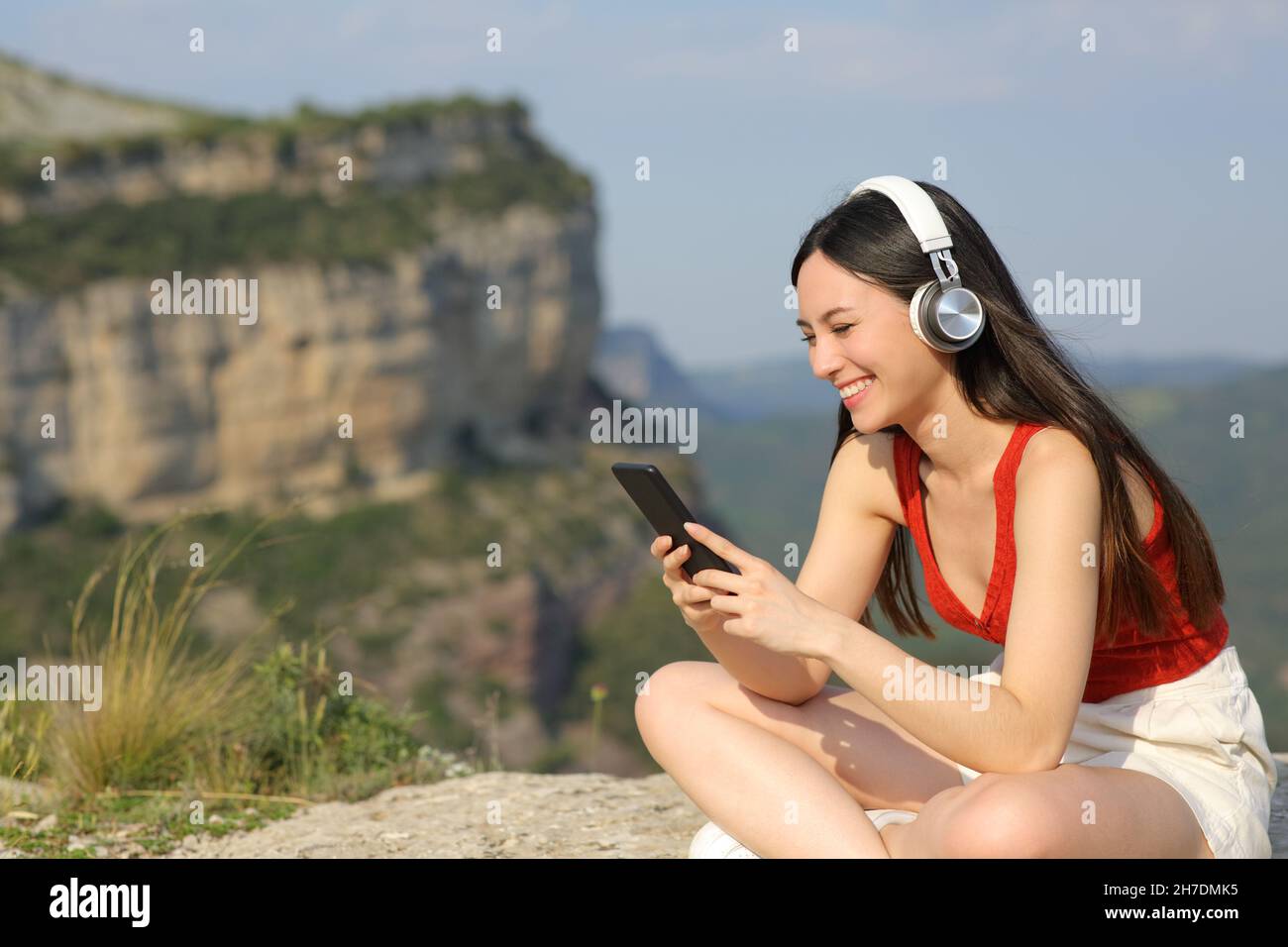 Happy asian woman wearing headphones listening to music in a cliff Stock Photo