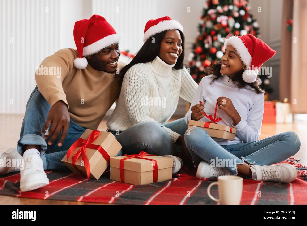 Cheerful black girl celebrating Christmas with family unwrapping gift box Stock Photo