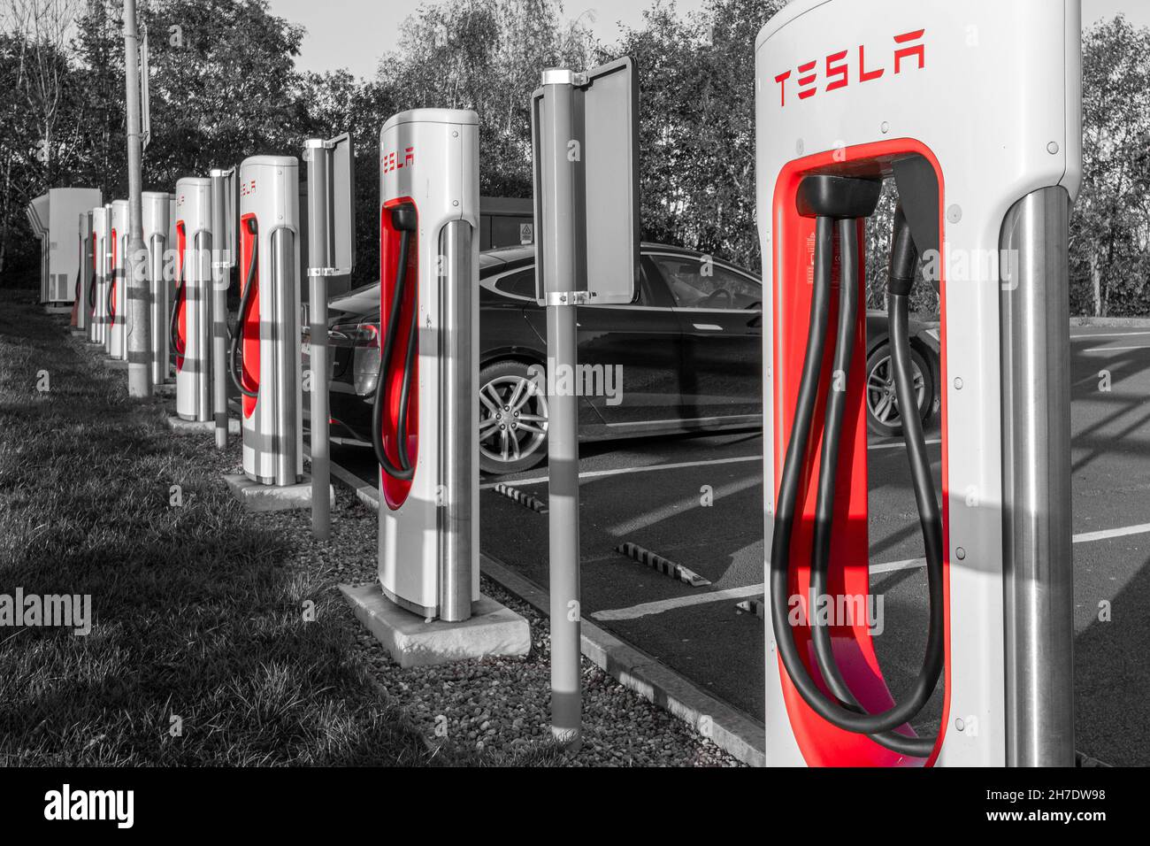 Tesla Supercharger station for charging electric cars vehicles at Telford Motorway Services, Shropshire, England, UK. Monochrome with colour splash Stock Photo