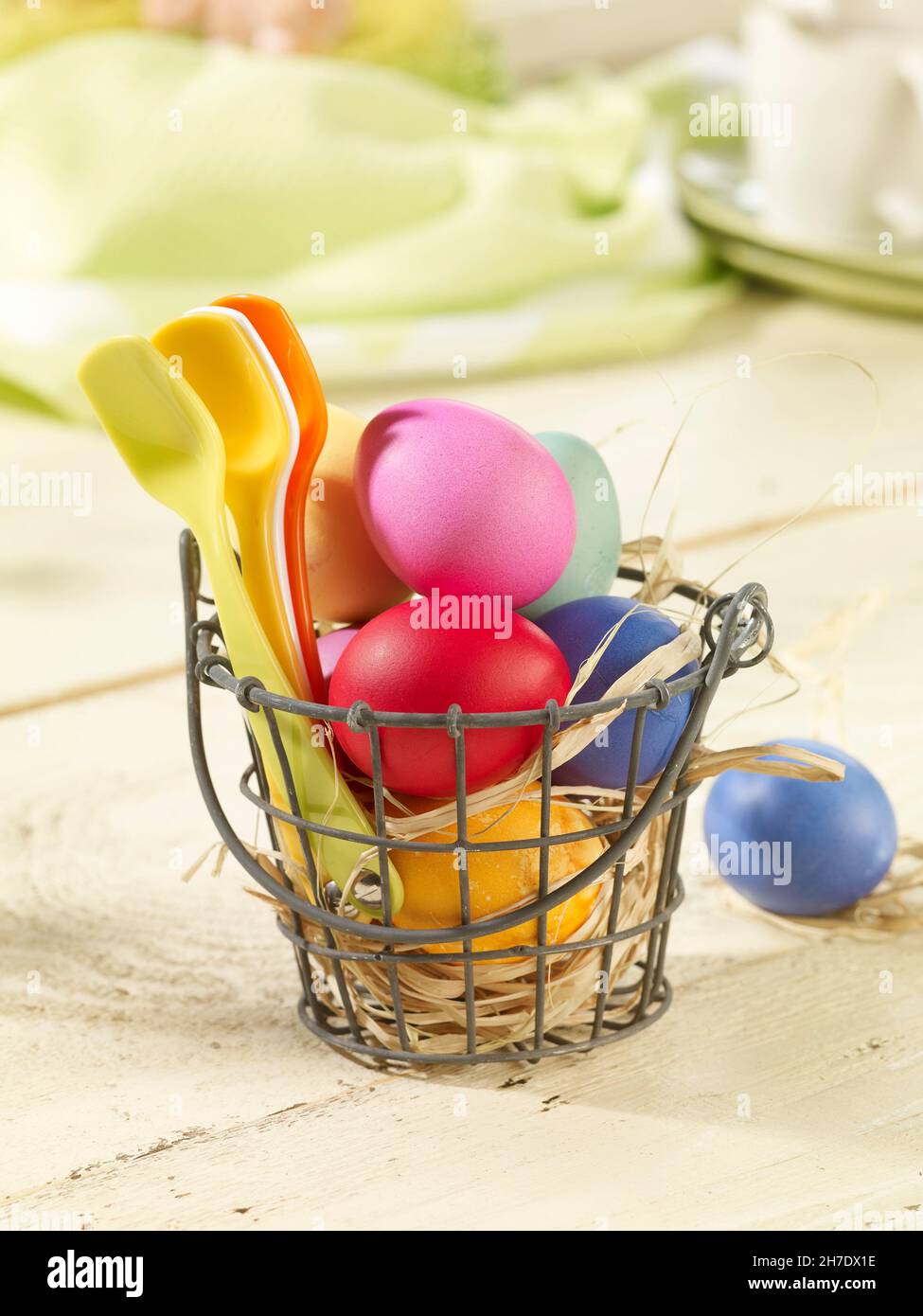 Colourful Easter eggs and plastic spoons in a wire basket lined with straw Stock Photo