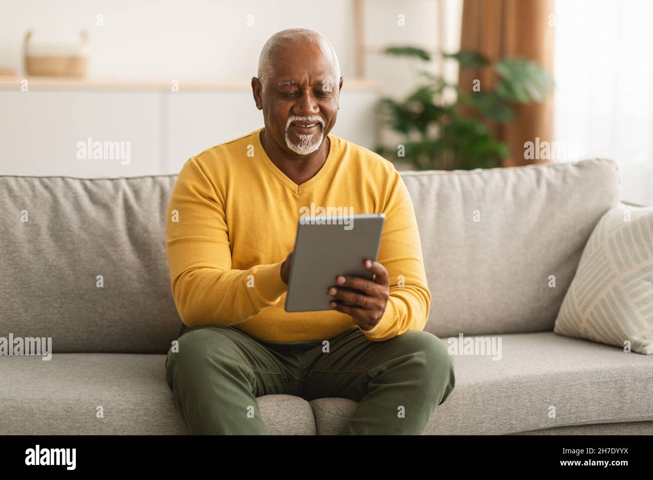 Senior Black Man Using Tablet Browsing Internet Sitting At Home Stock Photo