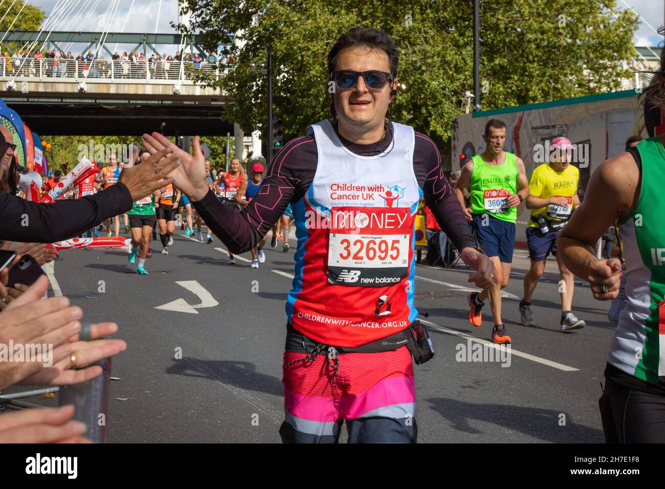 Man with sunglasses running doing high five with spectator, Virgin Money London Marathon 2021 at the 25 mile point, Victoria Embankment. Stock Photo