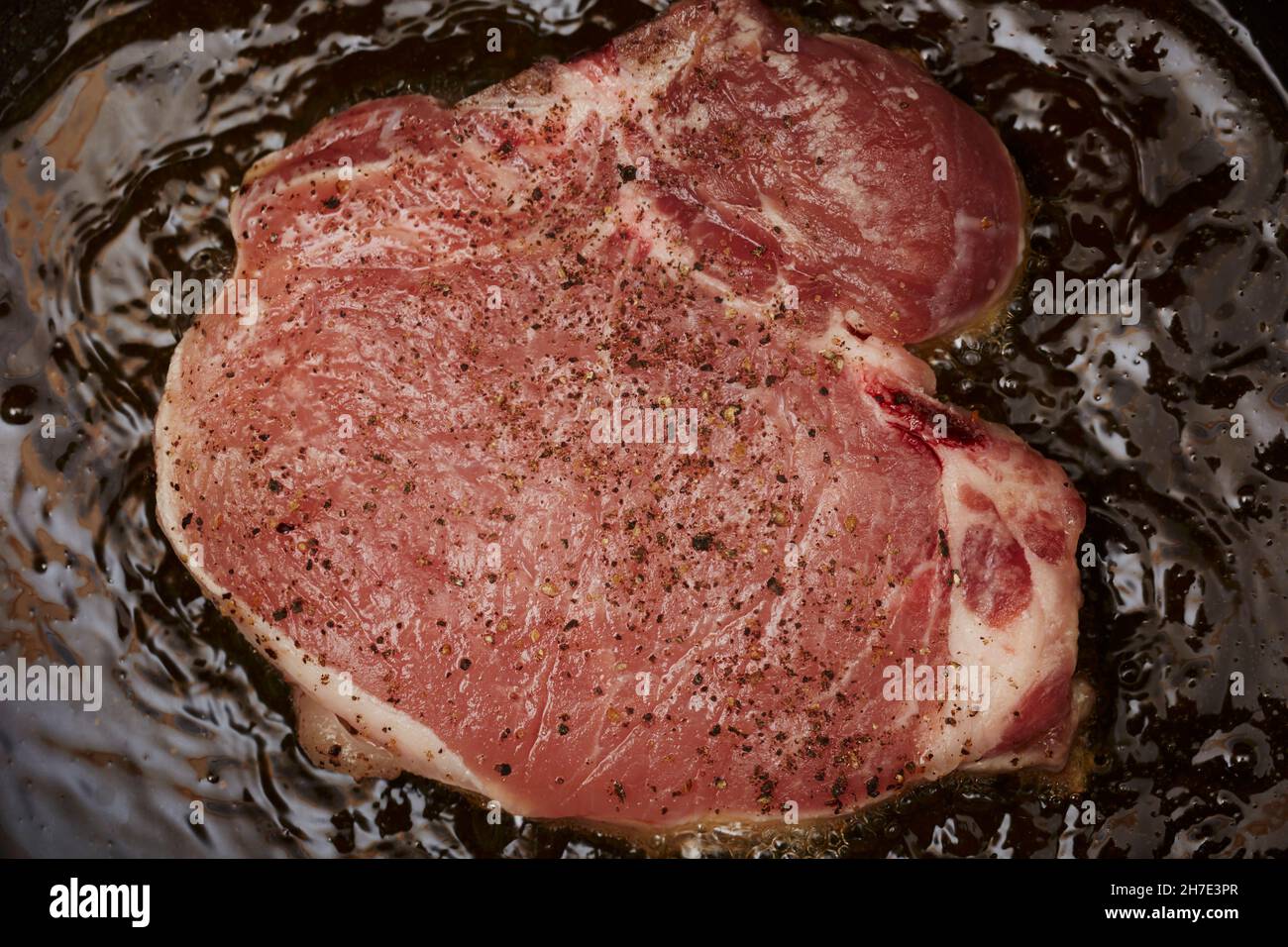 A pork chop seasoned with salt and pepper being fried in olive oil