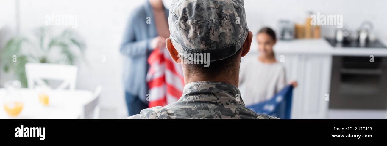 Man in military uniform near blurred family with american flag at home, banner Stock Photo