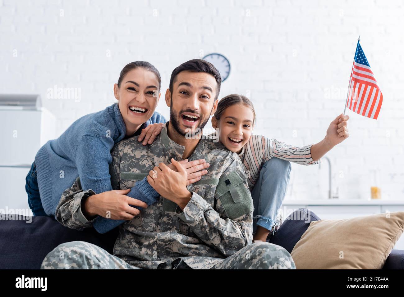 Positive family with american flag looking at camera near man in military uniform at home Stock Photo