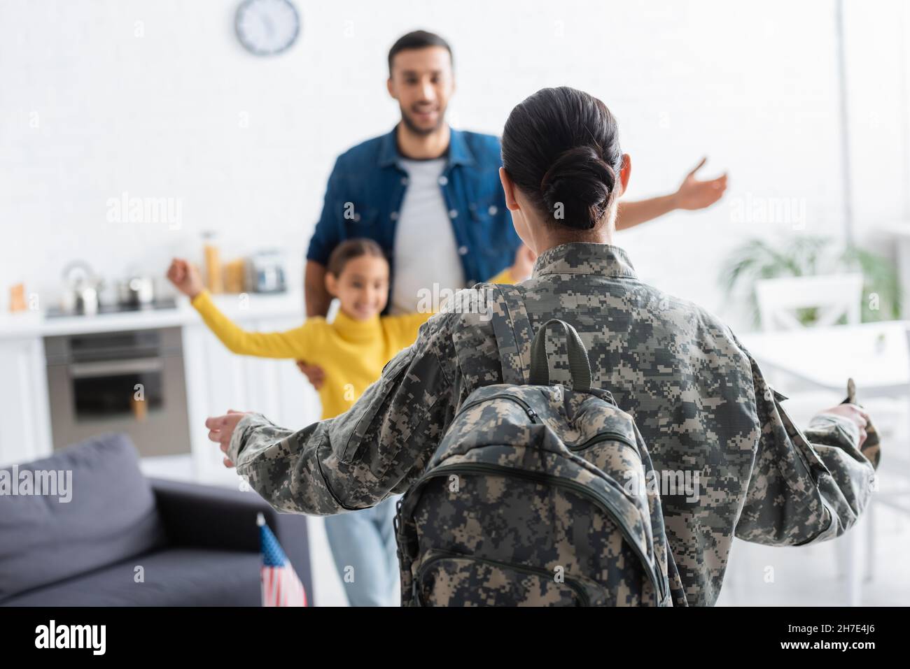 Woman in military uniform standing near blurred husband and daughter at home Stock Photo