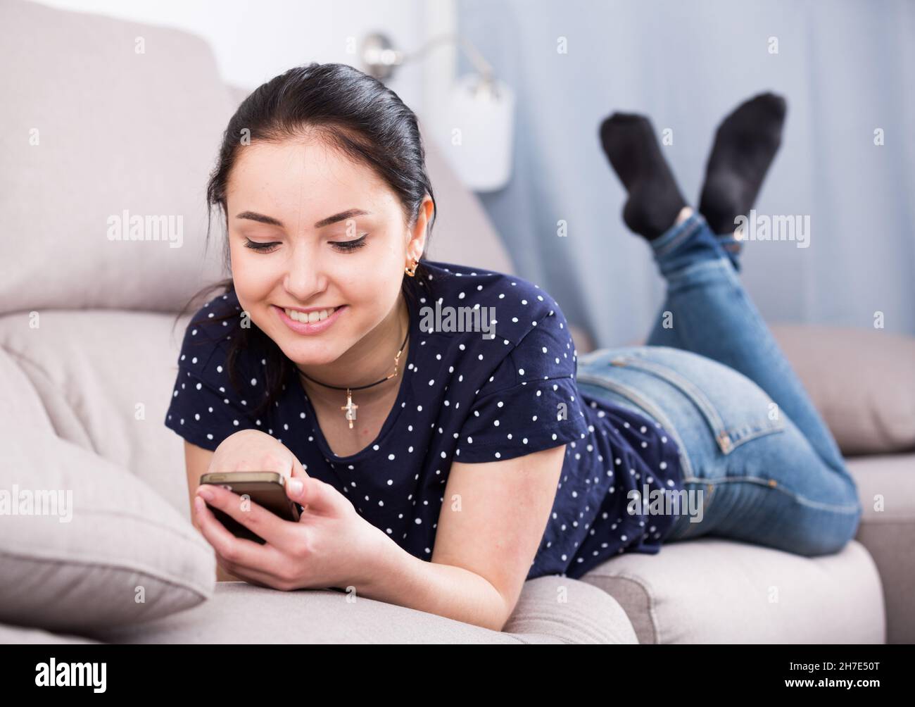 Happy woman on sofa with smartphone Stock Photo
