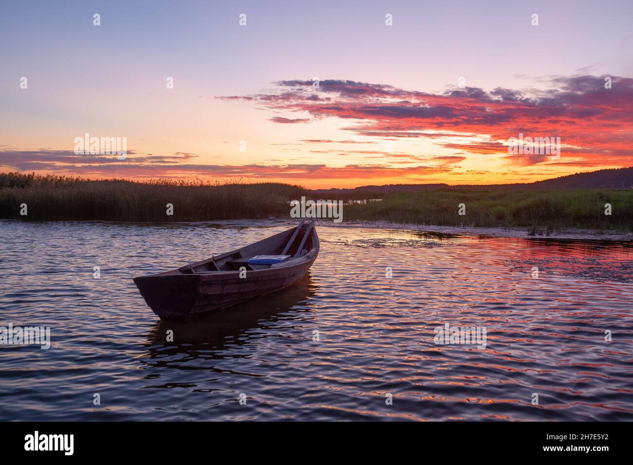 Lonely wooden boat in calm lake. Amazing sunrise in summer morning. The silhouette is reflecting on the water. Orange sky with clouds. Location place Stock Photo