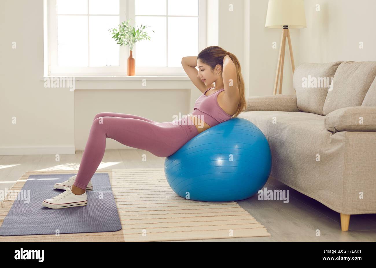 Happy fit young woman doing sit ups on exercise ball during fitness
