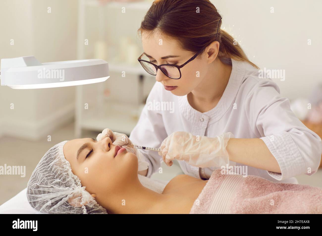 Specialist at clinic of aesthetic medicine injecting into lips of young woman Stock Photo