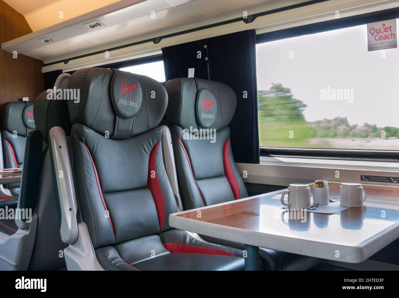 Virgin First Class logo brand quiet coach train seats on mainline route with table and coffee cups and scenery speeding past window, UK Stock Photo
