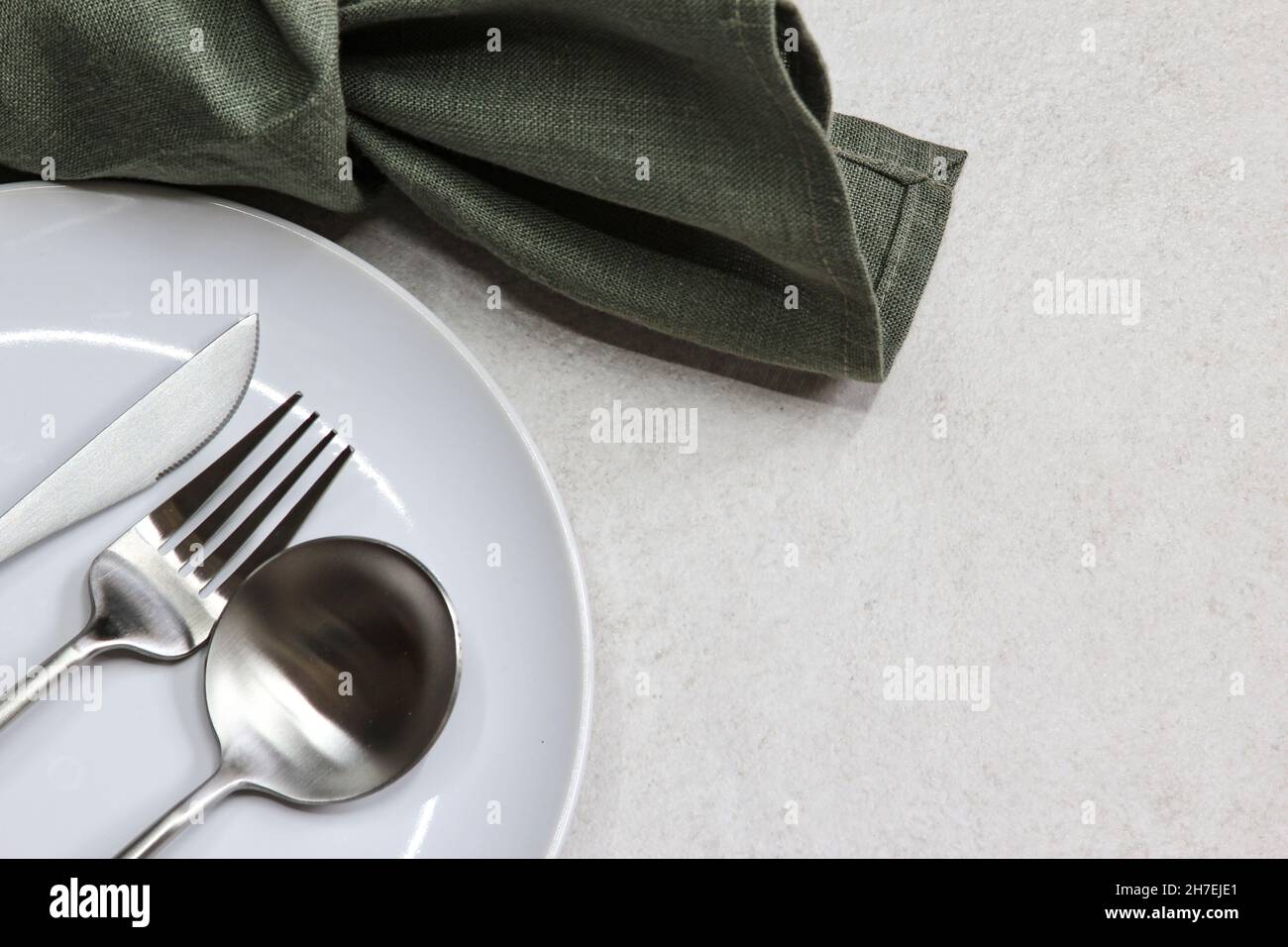 White empty plate with knife, spoons and fork green textile napkin on ...