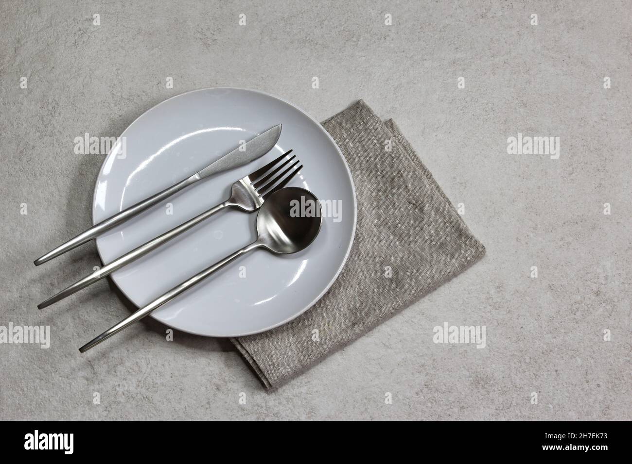 White empty plate with knife, spoons and fork gray textile napkin on ...