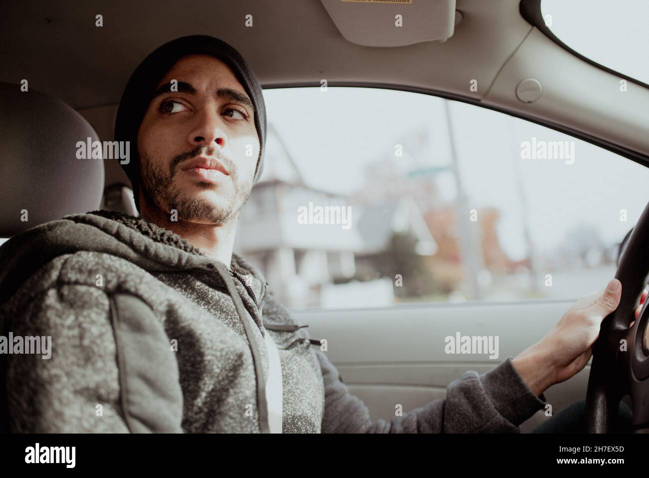 30-something mixed-race young millennial man driving in an older car to run errands. Serious expression while navigating Stock Photo
