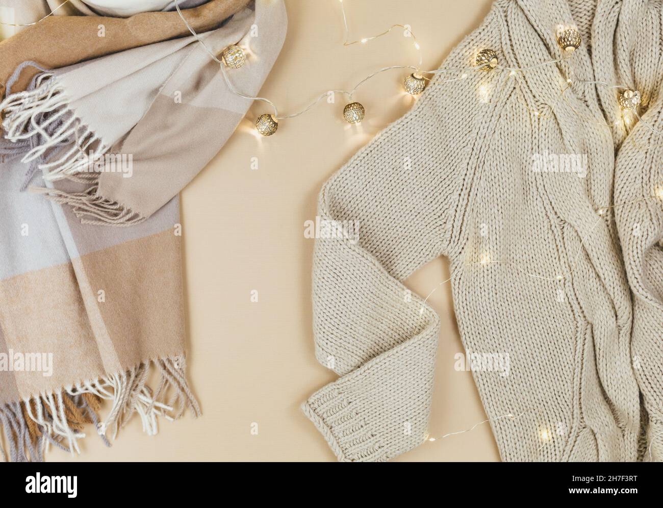 Women fashion winter clothes and accessories. Female look with knitted sweater, pullover, scarf, garlands on beige pastel background. Stock Photo
