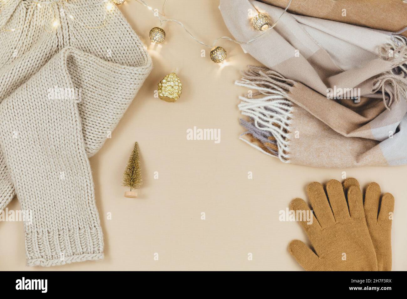 Women fashion winter clothes and accessories. Female look with knitted sweater, pullover, scarf, garlands on beige pastel background. Stock Photo
