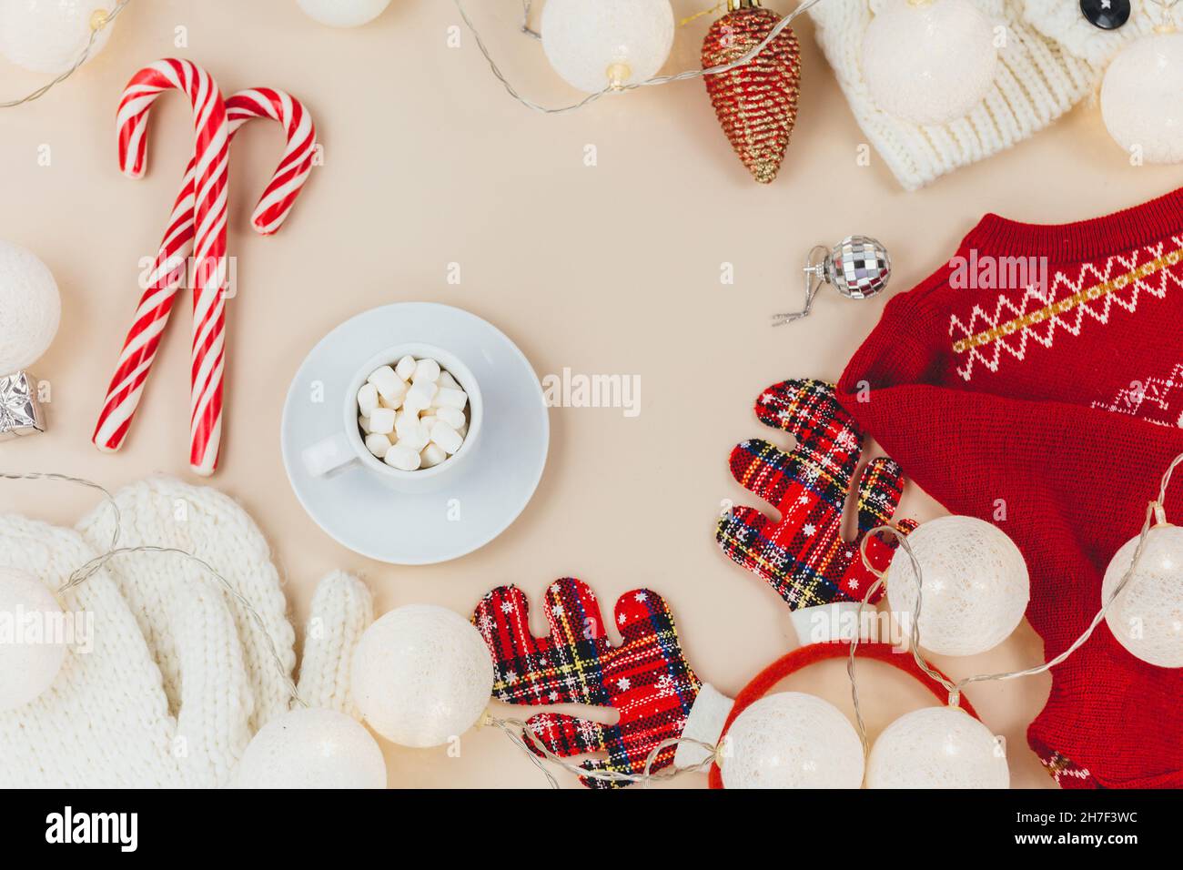 Cup of coffee, gift box and knitted sweaters, led lights on beige background. Hygge style, winter concept. Cozy home desk. New year and Christmas Stock Photo