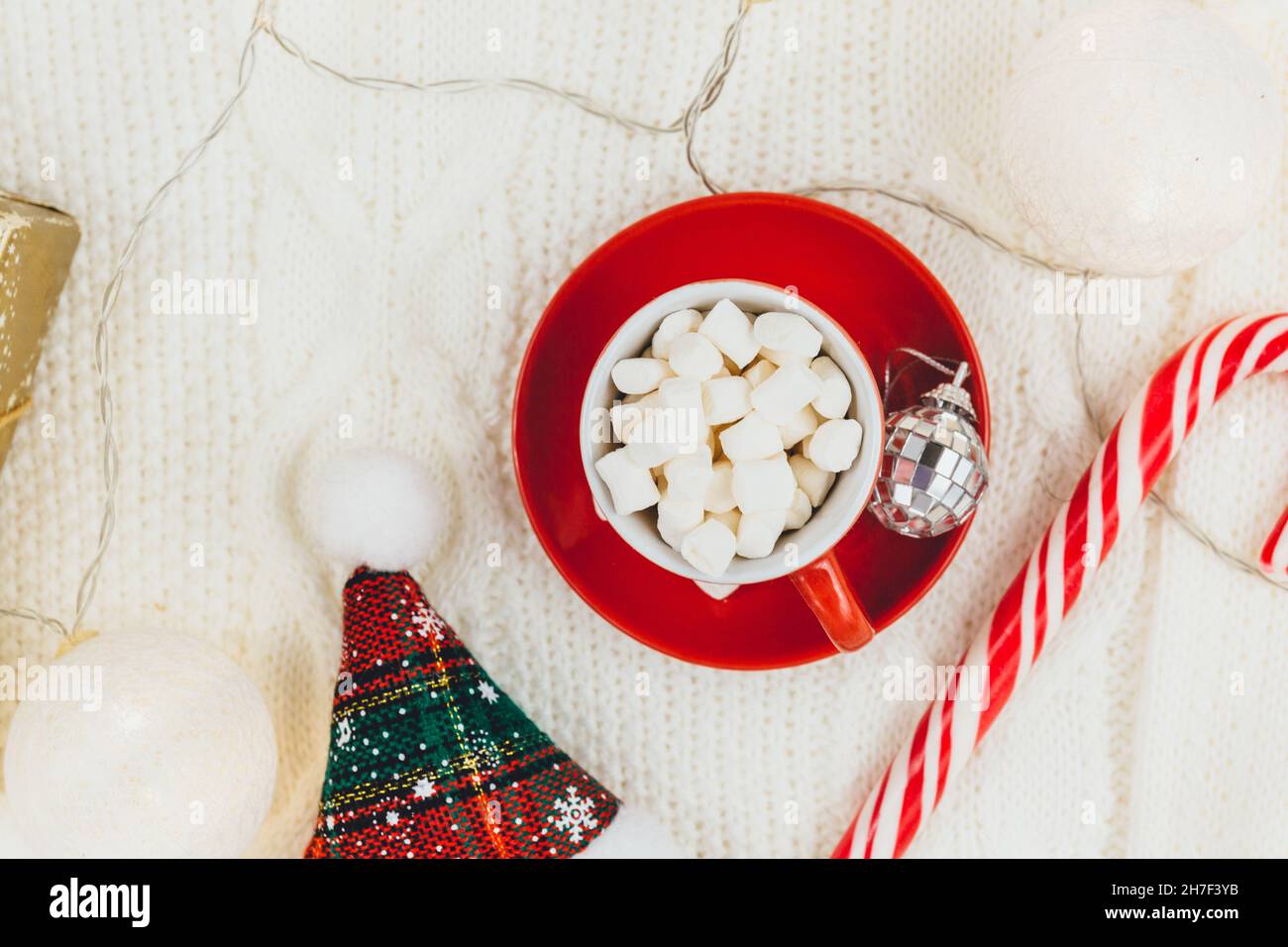 Cup of coffee, gift box and knitted sweater, led lights on beige background. Hygge style, winter concept. Cozy home desk. New year and Christmas Stock Photo