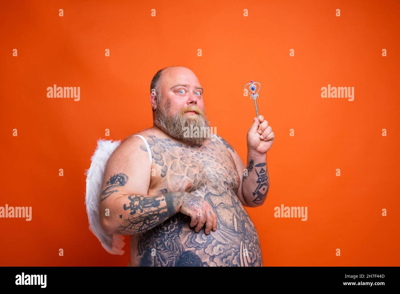 Fat thoughtful man with beard ,tattoos and wings acts like an magic fairy Stock Photo