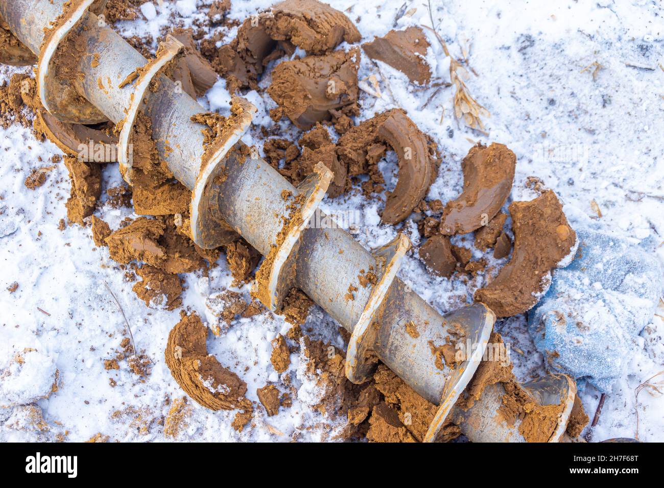a geological drill lies on frozen ground among pieces of clay cleaned from the working surface of the auger Stock Photo