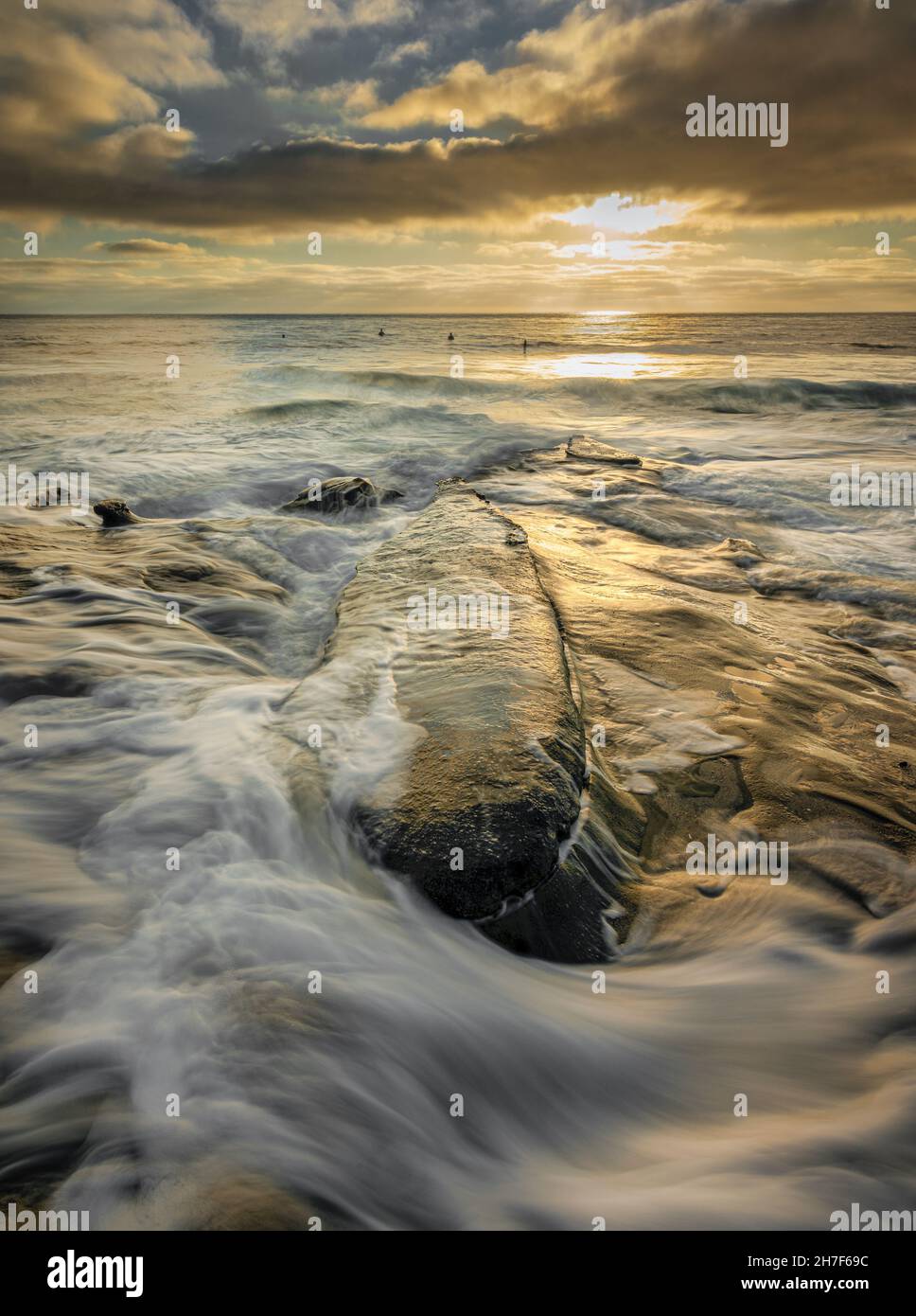 Waves hitting the rocks in La Jolla, California, silhouetted surfers  Stock Photo