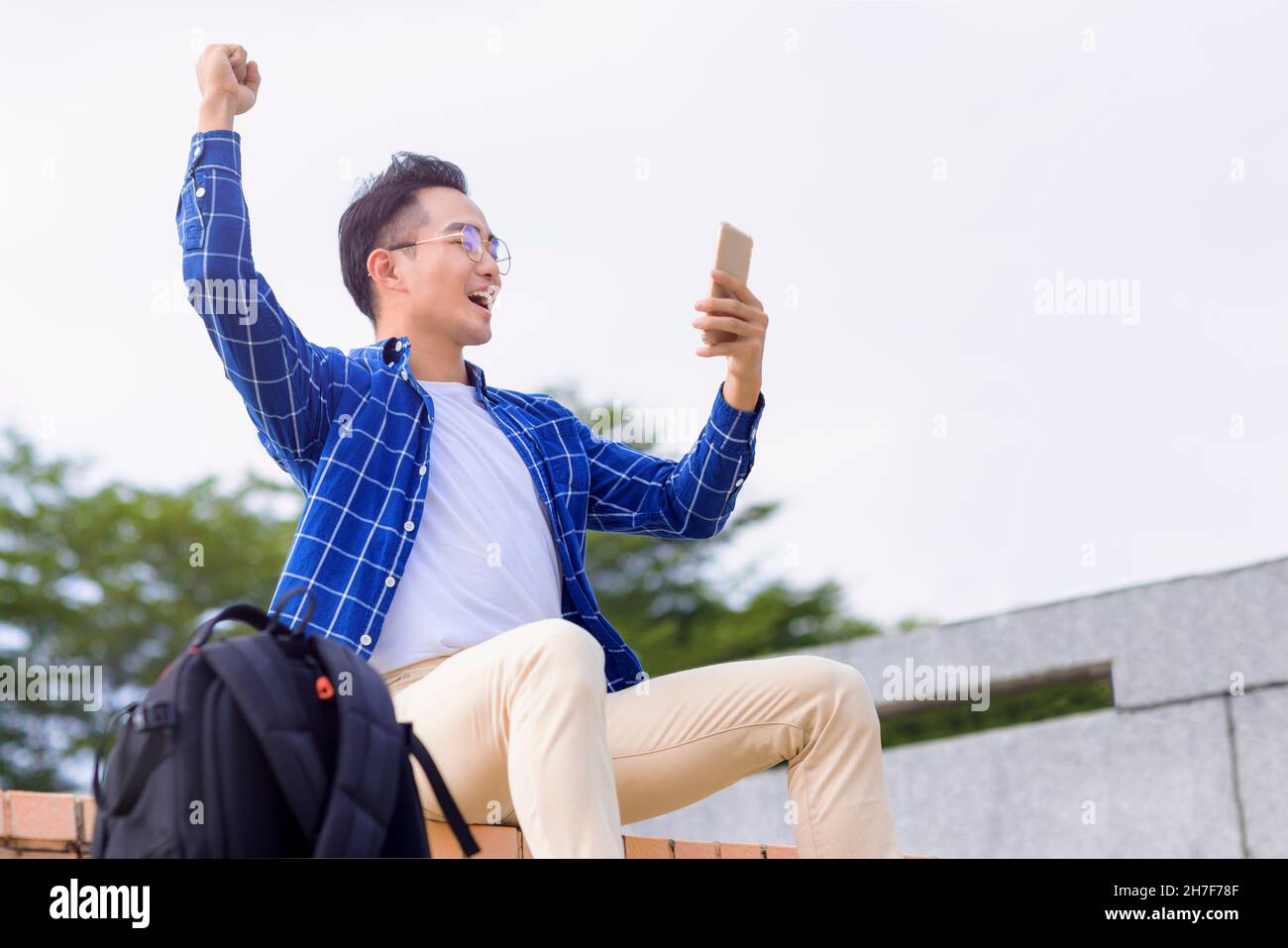 excited young asian man sitting on stairs and using smart phone Stock ...