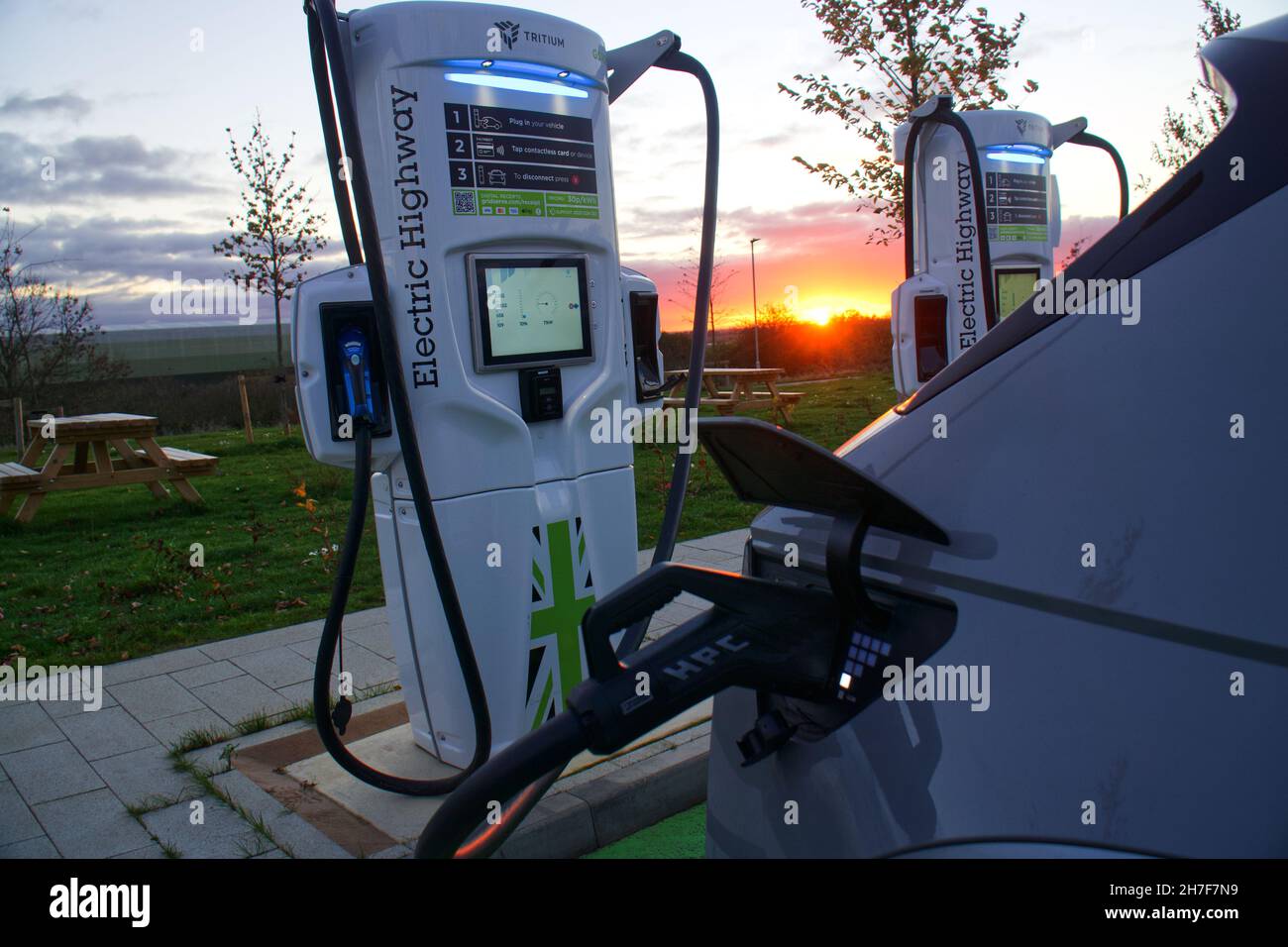 Electric vehicle plugged in and charging at sunset at a Gridserve Electric Highway high power charger in Rugby, England Stock Photo