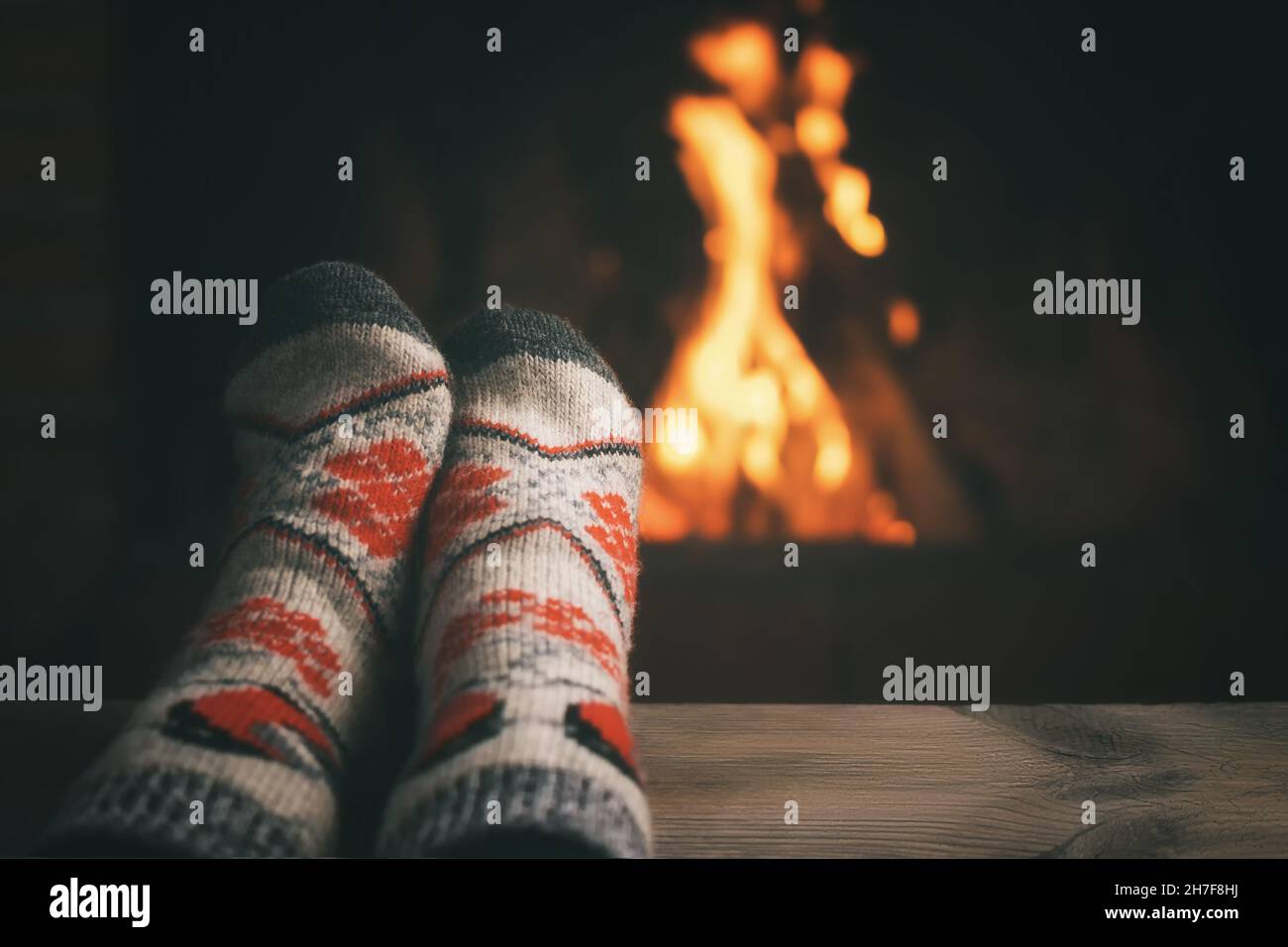 Girl resting and warming her feet by a burning fireplace in a country house on a winter evening. Stock Photo