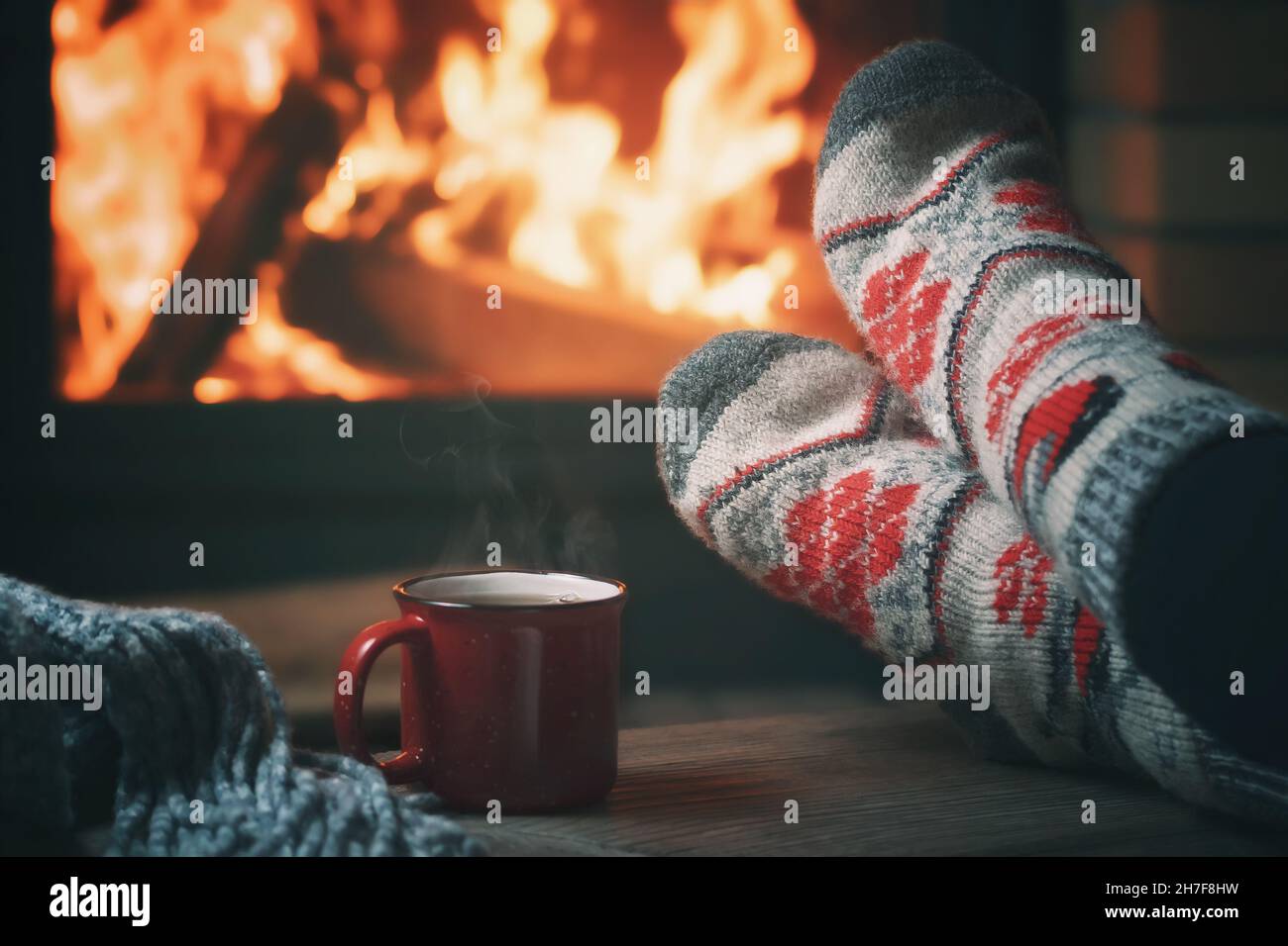 Girl resting and warming her feet by a burning fireplace in a country house on a winter evening. Stock Photo