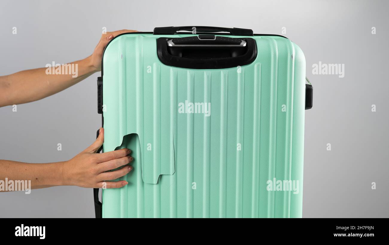 A woman demonstrates a broken suitcase on a white background. Damaged