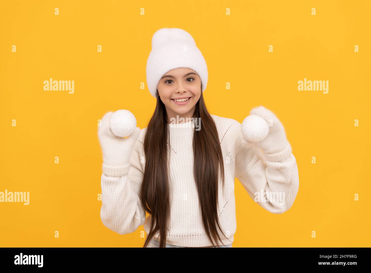 happy teen girl ion winter hat and gloves hold snowballs on yellow background, christmas Stock Photo