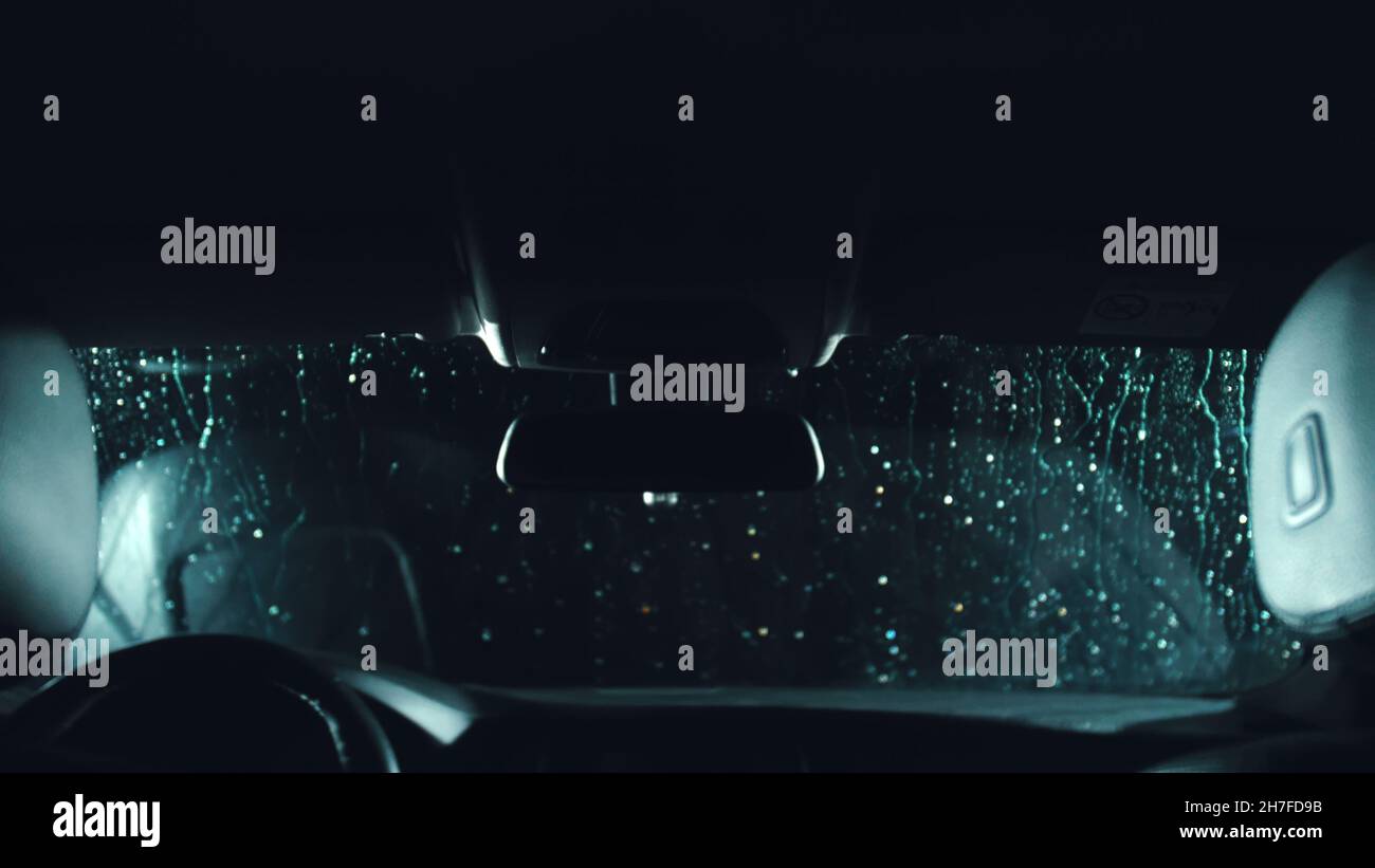 Drops flow down the windscreen. Inside view of a windshield car. Dark black cinematic picture. Process stage of polishing and washing a auto. Movement Stock Photo