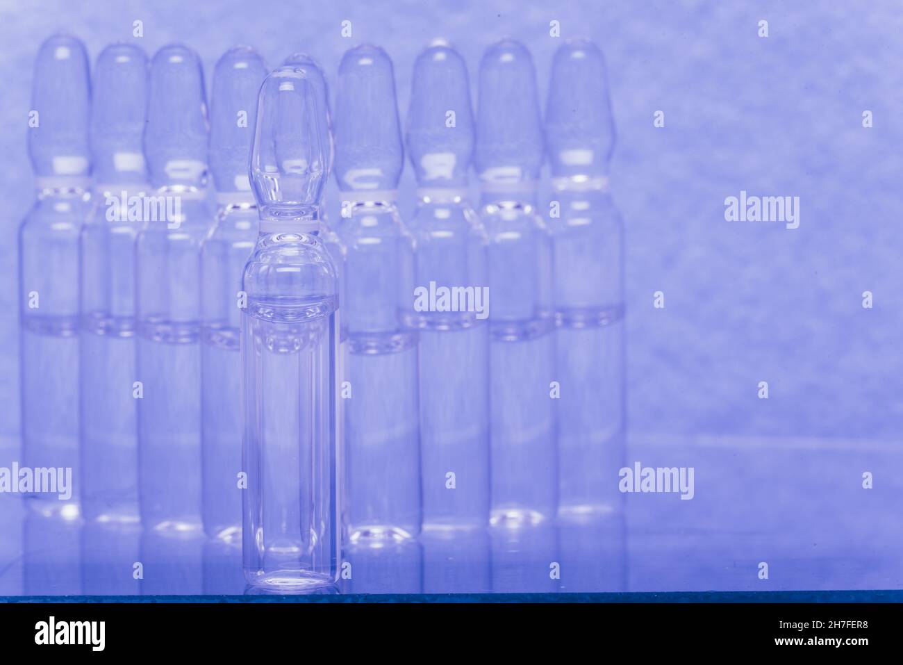 Glass medical ampoule vial for injection. Medicine is liquid sodium chloride with of aqueous solution in ampulla. Close up. Bottles ampule multicolor Stock Photo