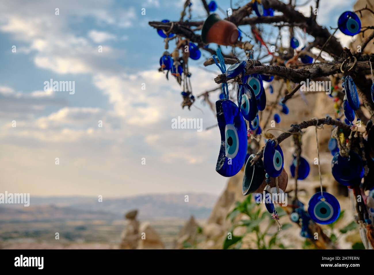large groups of blue bead worn against the evil eye hanging on trees in edge castle (uchisar) in Cappadocia, gore in Turkey with dramatic cloudscape Stock Photo