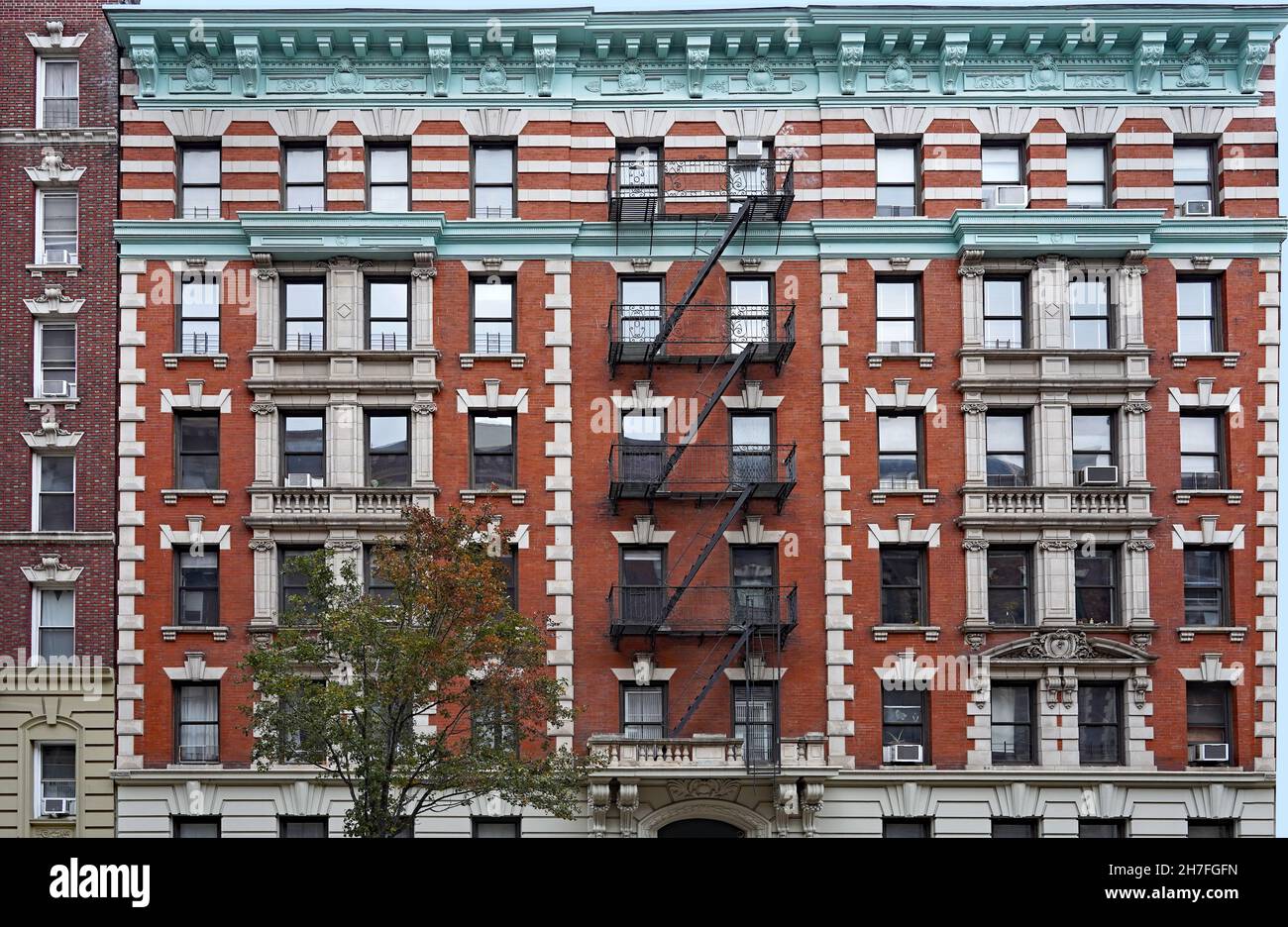 Old fashioned Manhattan apartment building facade with ornate roof cornice and external fire escape ladders Stock Photo