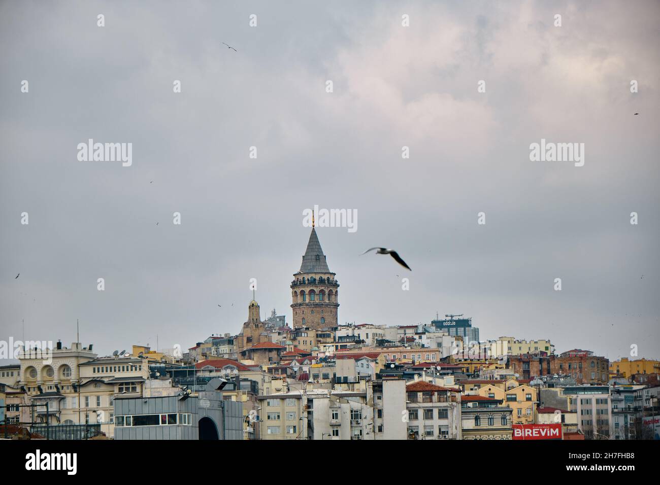 Famous galata tower during overcast and rainy day by taking photo from eminonu district behind the many local apartments and Turkish flags Stock Photo