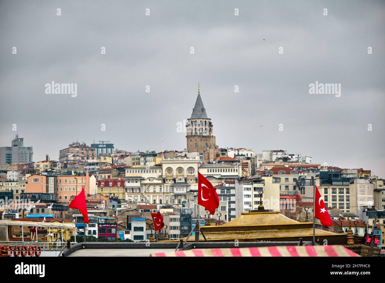 Famous galata tower during overcast and rainy day by taking photo from eminonu district behind the many local apartments and Turkish flags Stock Photo