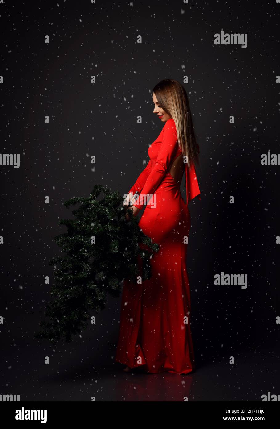 Young glamour woman in long red dress with winter christmas fir tree under heavy snow. New year concept  Stock Photo