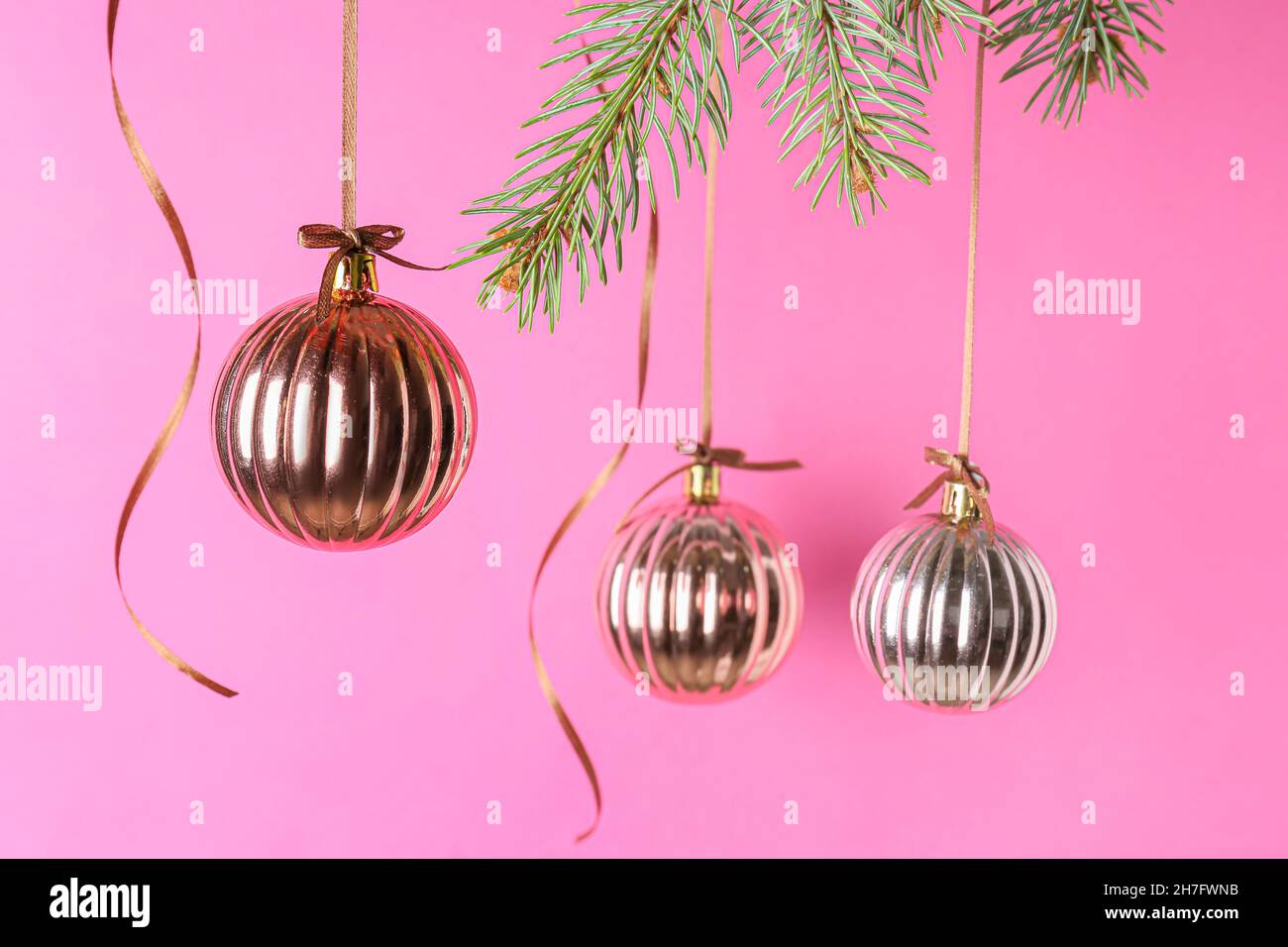 Christmas balls hanging on fir branches against pink background