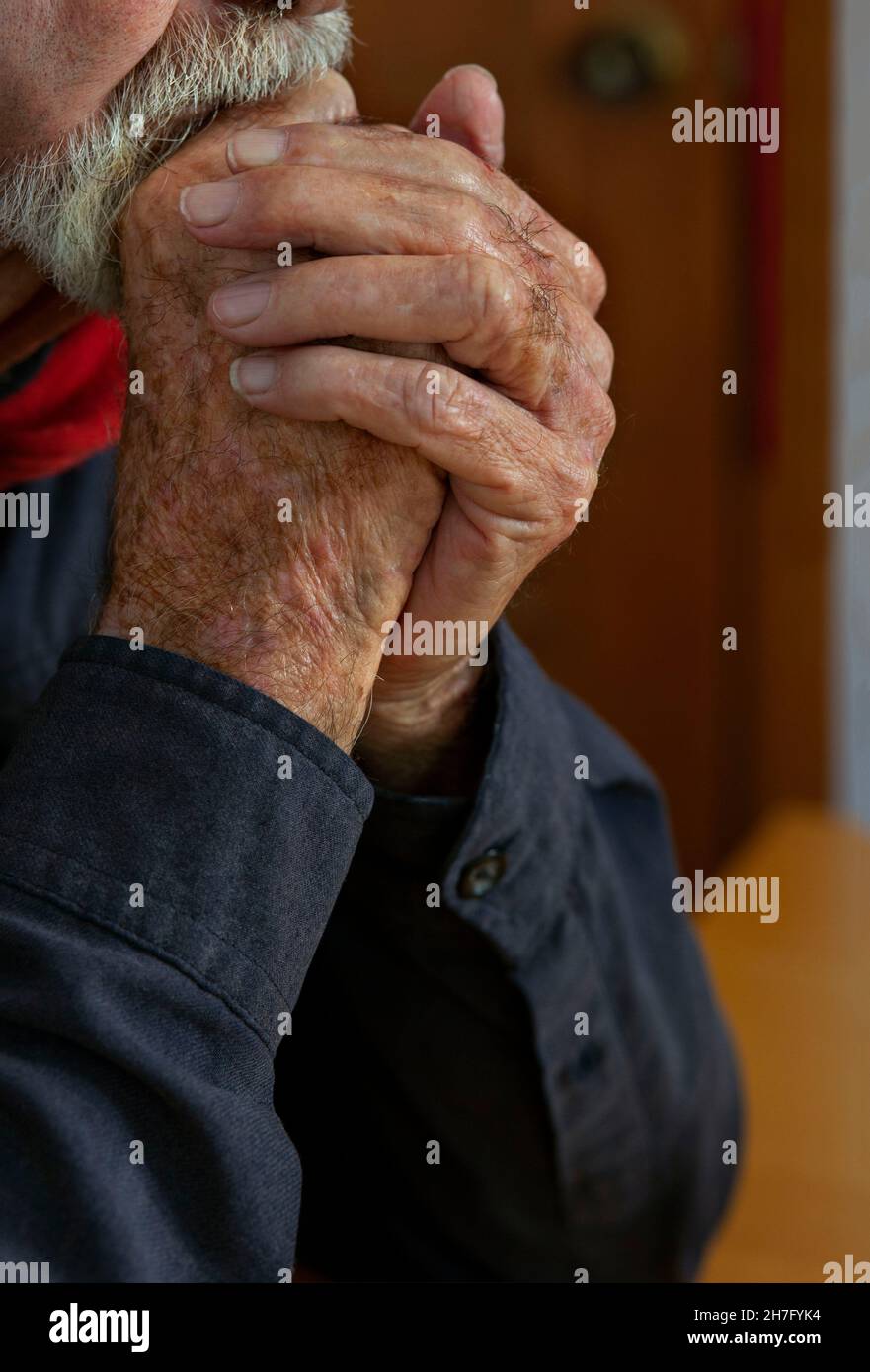 A close up of the hands of an elderly man's hands clasped against his chin MR - Model Released Stock Photo