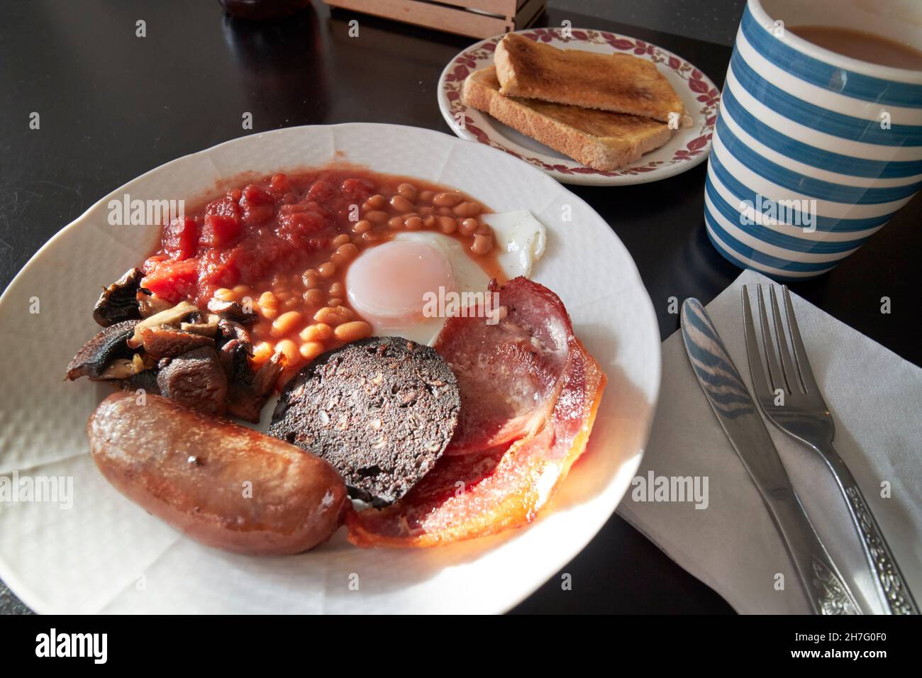 low cost cafe fried english breakfast egg bacon sausage black pudding beans tomatoes and mushrooms with toast and tea New Brighton the Wirral merseysi Stock Photo