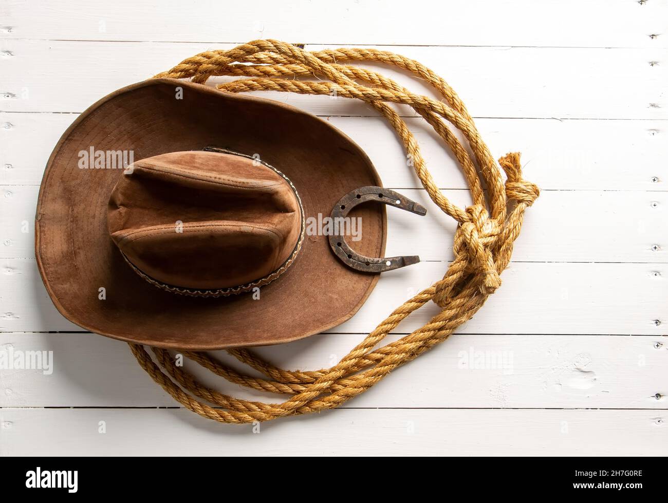 Classic brown cowboy hat lasso and horseshoe wild west still life on rough white wooden table Stock Photo