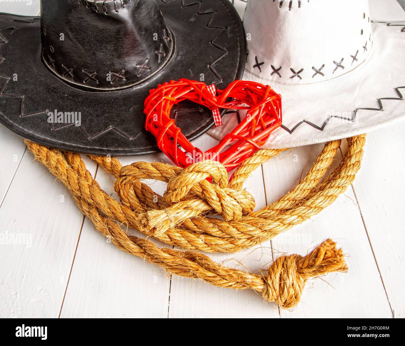 Conceptual image of a rural wedding of cowboys. White bride hat and dark groom hat and red heart symbol of love Stock Photo