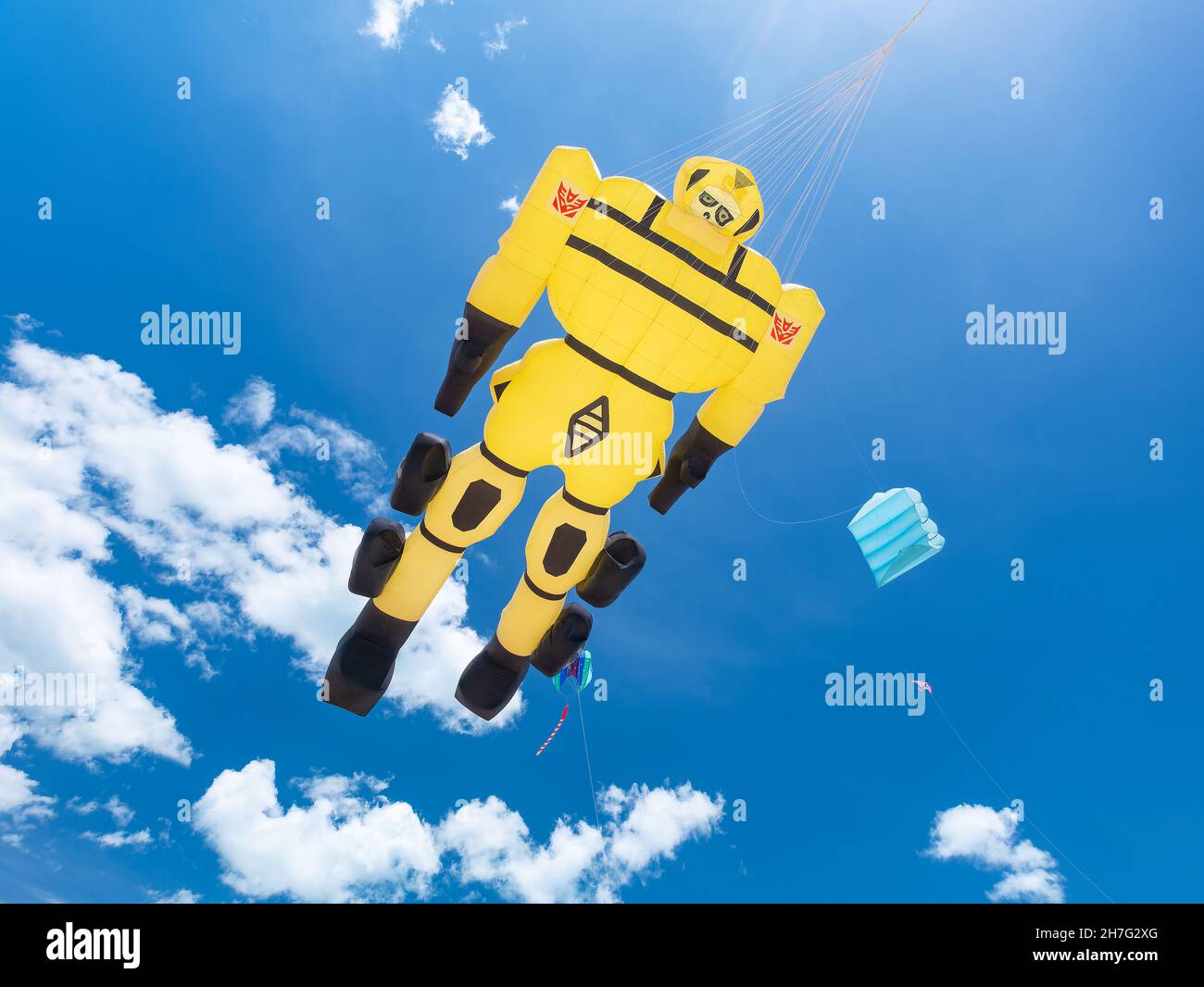 Large, yellow, inflatable kite shaped as a Transformer toy flying against a blue sky background at Surat Thani Kite Festival, 2-4 April in Surat Thani Stock Photo
