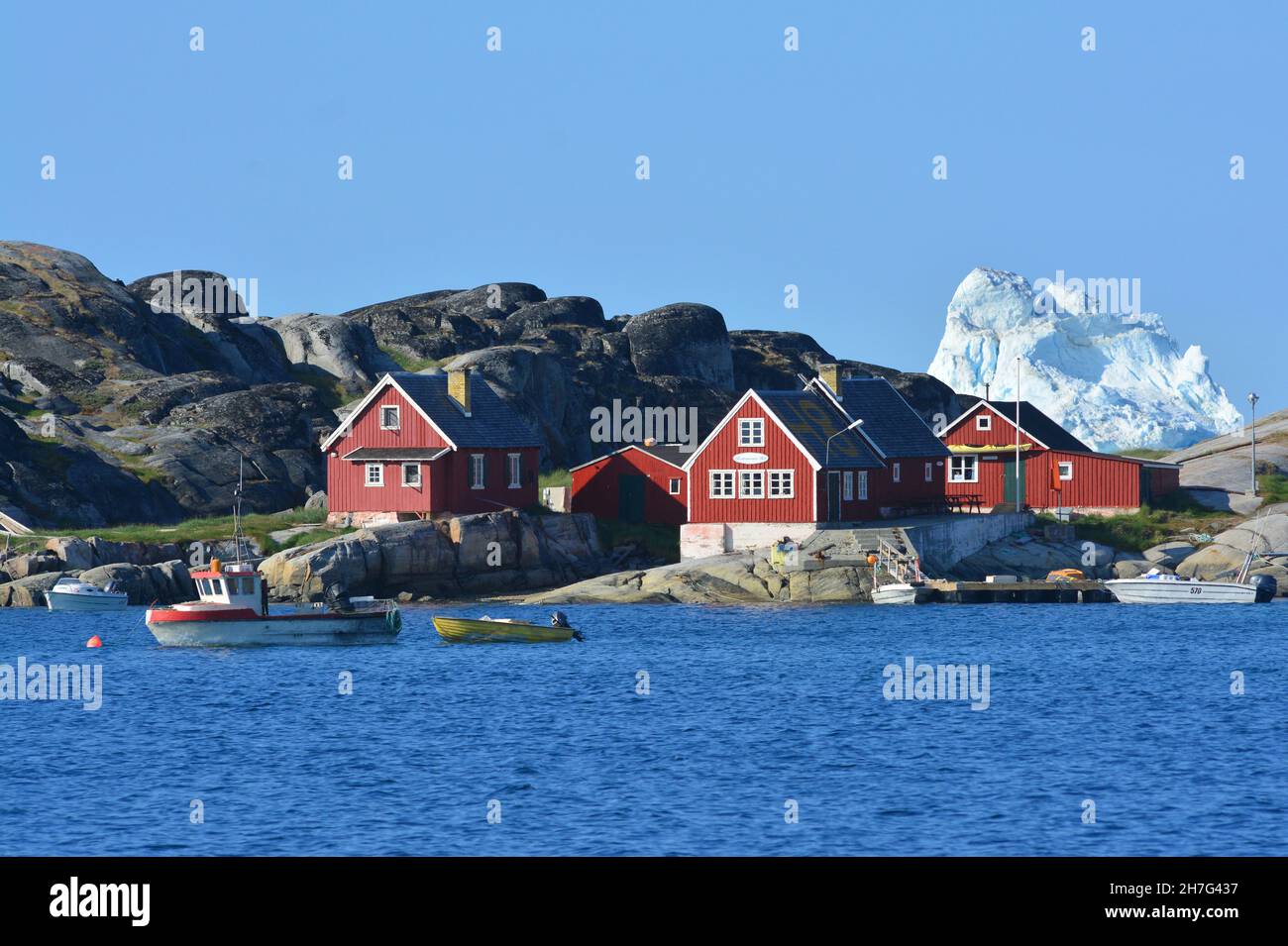 DENMARK. GREENLAND. WEST COAST. OQAATSUT BAY. ICEBERG BEHIND THE  HOUSES OF THE VILLAGE OF OQAATSUT, FORMER WHALE HUNTING STATION. Stock Photo
