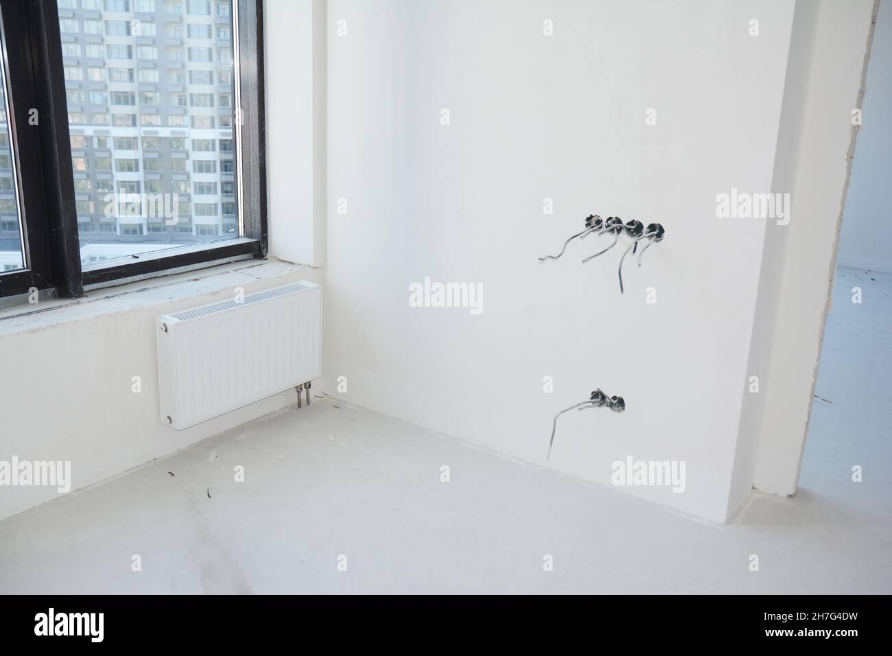 A modern room renovation with white walls and radiator, and a black window frame. Incomplete installation of electrical sockets, plugs, and switches a Stock Photo