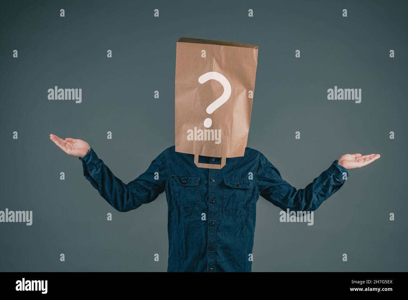 A young man has a paper bag on his head with a question mark, asking why, looking for answers, dark background Stock Photo