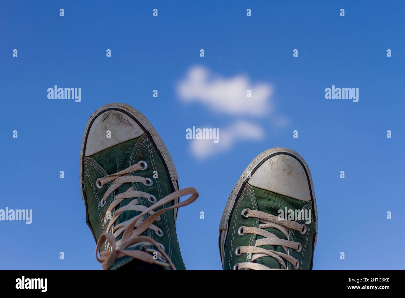 old green sneakers on a background of blue sky with clouds, vacation concept Stock Photo