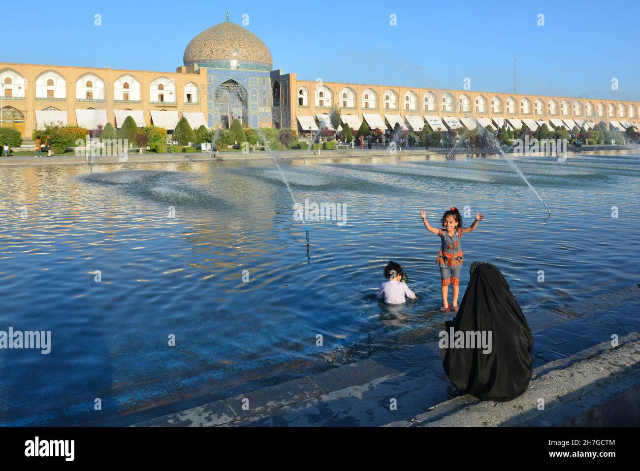 IRAN. ISPAHAN ESFAHAN. EMAM SQUARE. WOMAN IN VEIL LOOKING HER KIDS PLAYING WITH THE WTAER IN THE FOUNTAIN FACING THE CHEICK LOFTOLLAH MOSQUE. Stock Photo