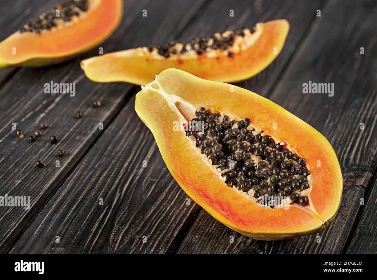 Several pieces of ripe papaya on a wooden table. Quarters of papaya on a dark plank table. Stock Photo
